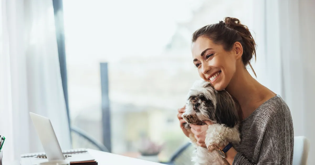 Pet owner at home with a small dog during a telehealth appointment on a laptop