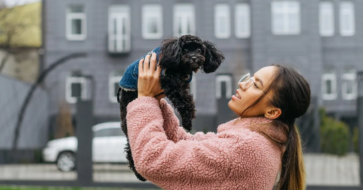 Renter holding up a small black puppy outside an apartment building