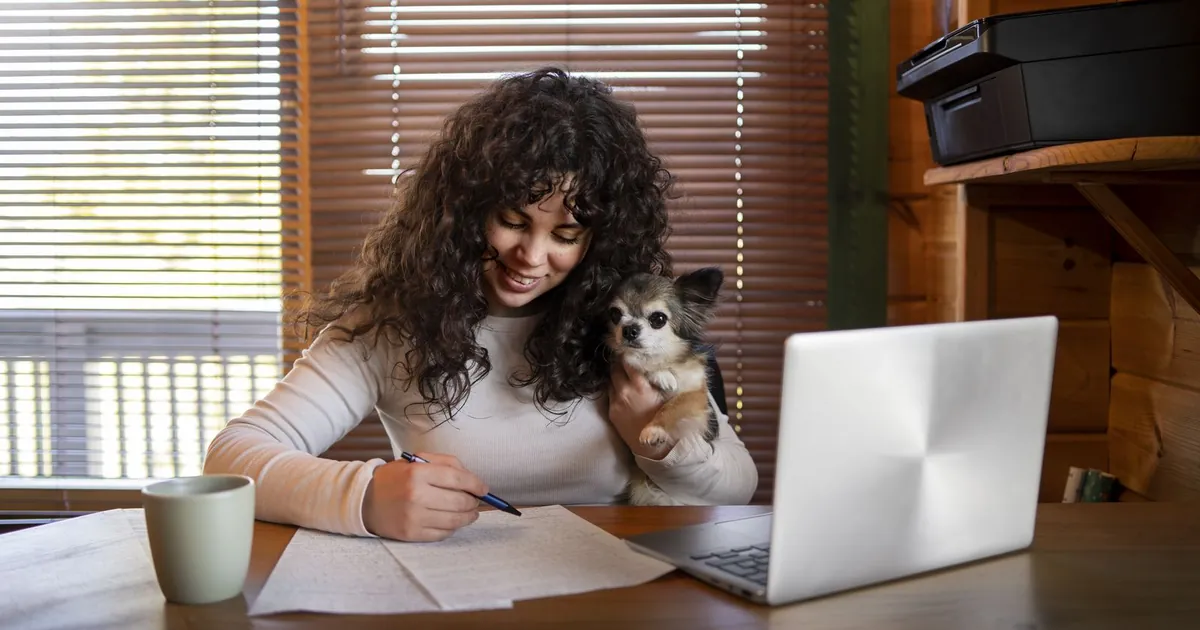 Tenant holding a small dog while filling out housing paperwork at a desk with a laptop