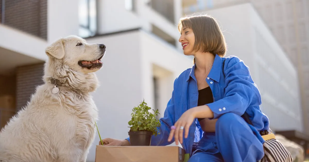 Smiling woman crouching beside a large white dog outside an apartment building
